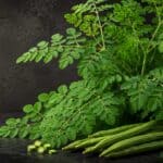 Premium Moringa (Moringa oleifera) leaves and fresh drumstick pods on a black botanical background with soft golden light.