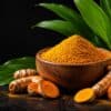 Premium Turmeric (Curcuma longa) roots with a wooden bowl of turmeric powder and fresh green leaves on a black background.